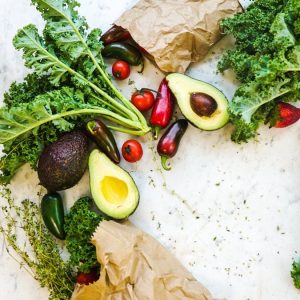 Avocado, kale, and more fresh produce artfully arranged on a marble surface.